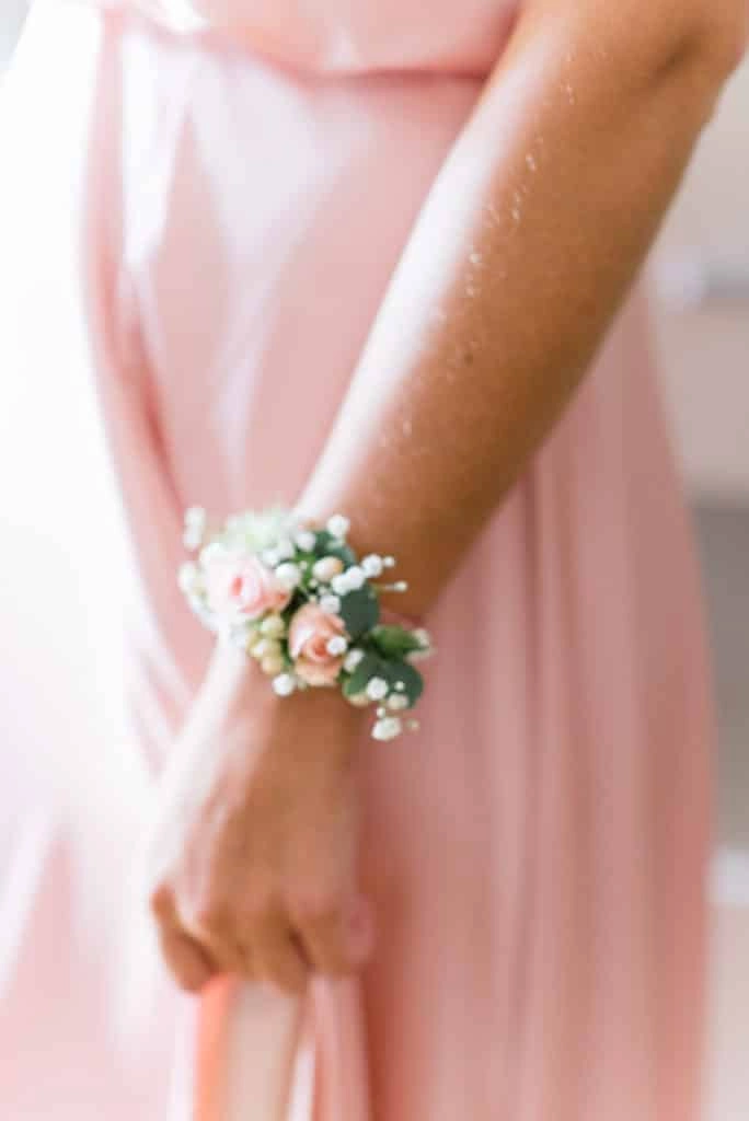 Blumenarmband vor einem rosa Kleid.