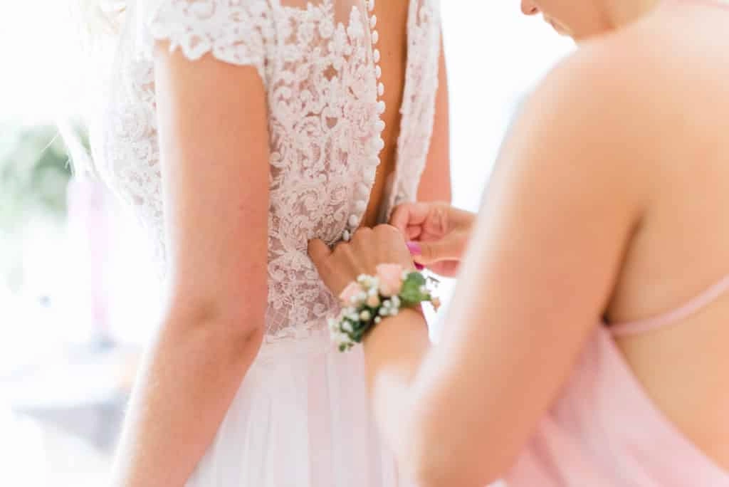 Helfende Hände schließen den Rücken des Brautkleids.
