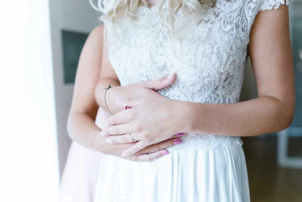 Hände der Braut vor ihrem Spitzenkleid.