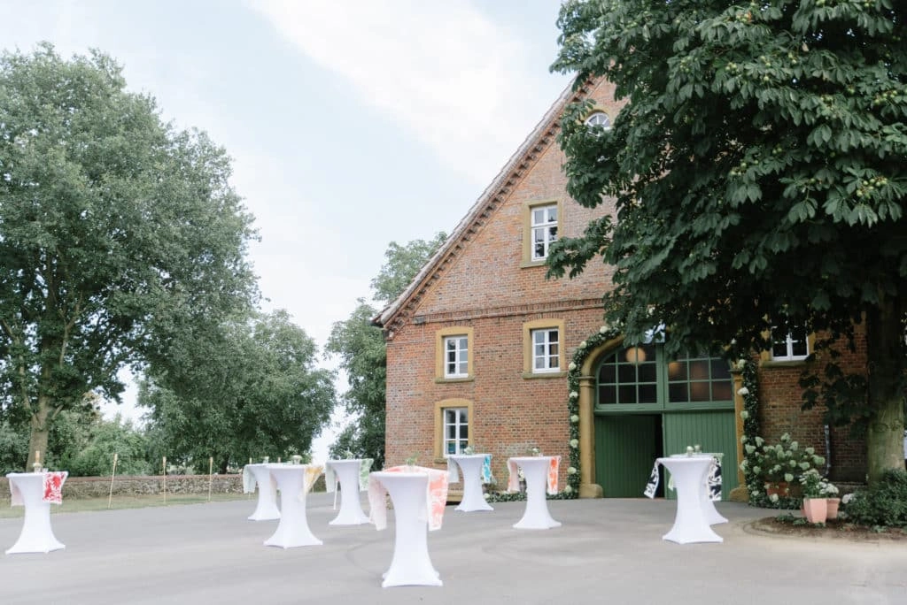 Stehtische stehen vor einem Backsteinhaus für den Hochzeitsempfang bereit.
