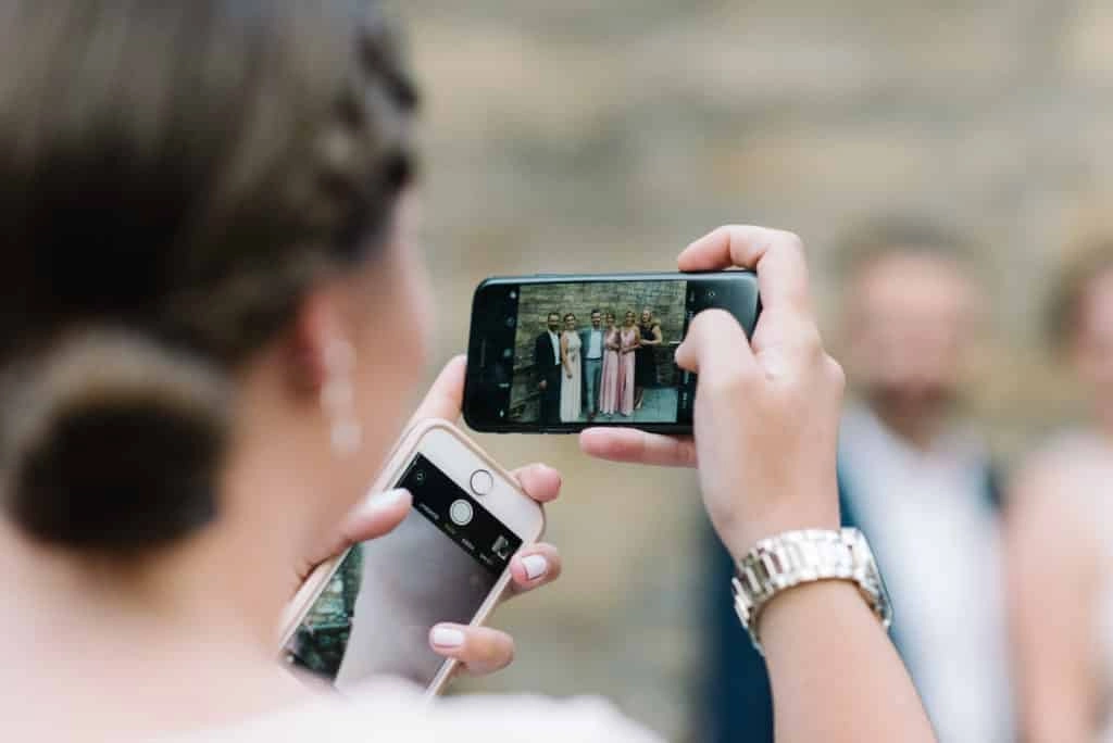 Gast fotografiert das Brautpaar mit dem Smartphone.