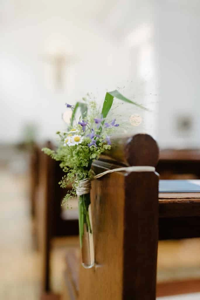 Kleine Blumenvase an einer Kirchenbank.