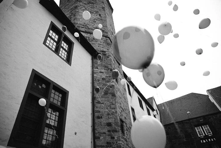 Luftballons steigen zwischen historischen Gebäuden auf, in Schwarz-Weiß.