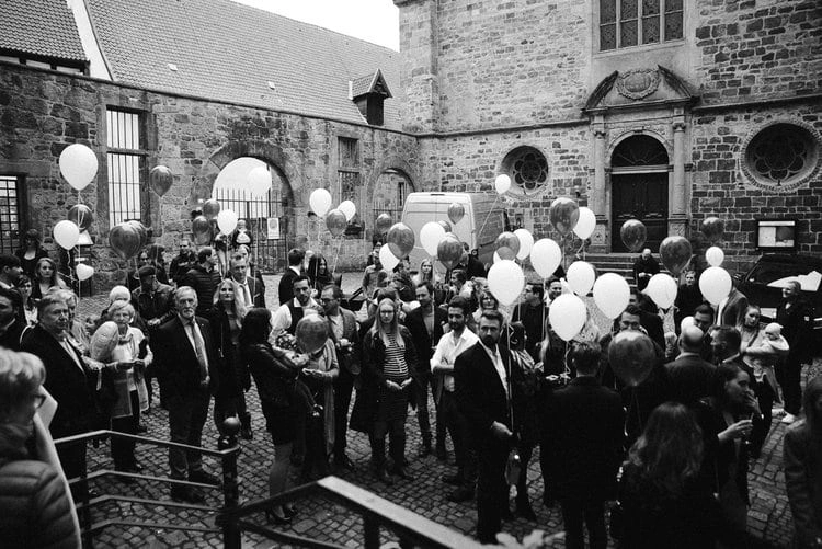 Hochzeitsgesellschaft mit Luftballons im Innenhof, in Schwarz-Weiß.