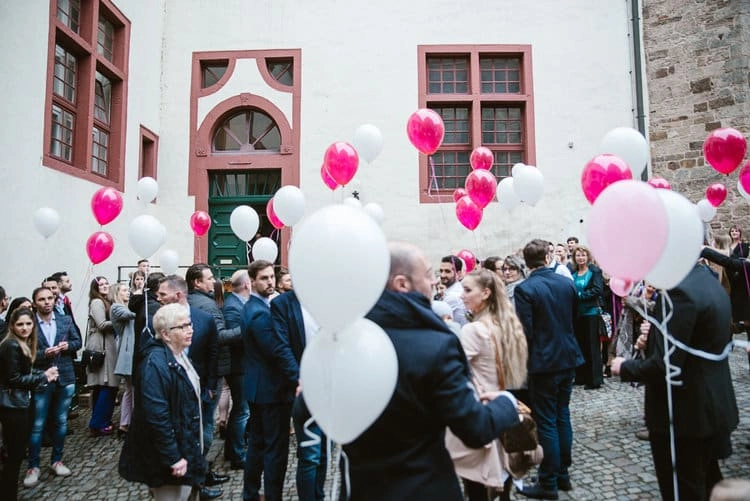 Gäste halten rosa und weiße Luftballons im Hof.