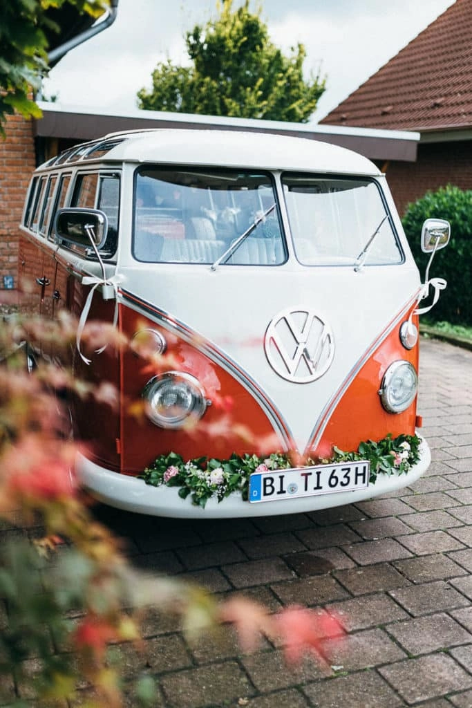 Orange-weißer Oldtimerbus mit Blumenschmuck.