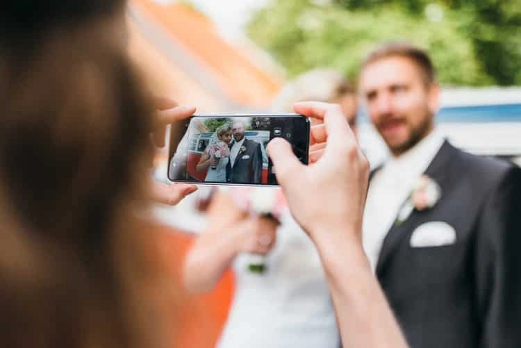 Gast fotografiert den Bräutigam mit dem Smartphone.