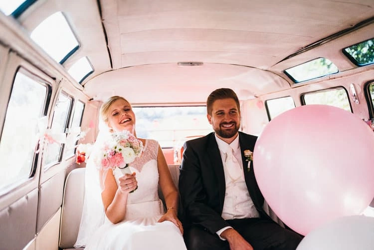 Brautpaar mit Getränken und rosa Ballon im Bus.