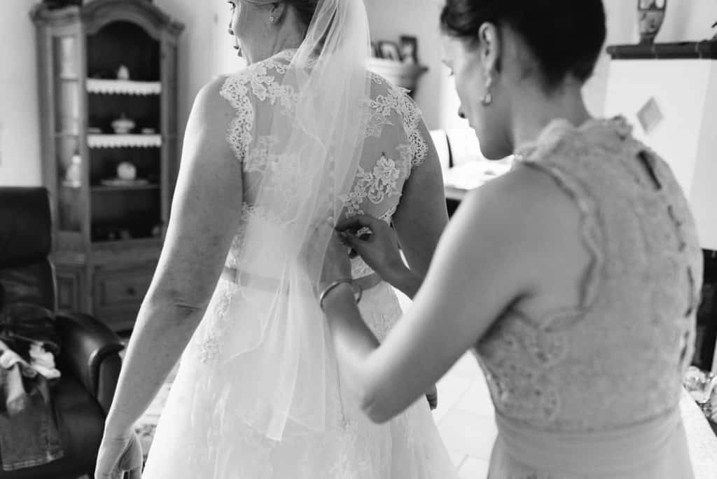 Braut bekommt Hilfe beim Anziehen des Kleids, in Schwarz-Weiß.