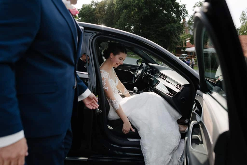 Die Braut steigt im Hochzeitskleid aus einem Auto.
