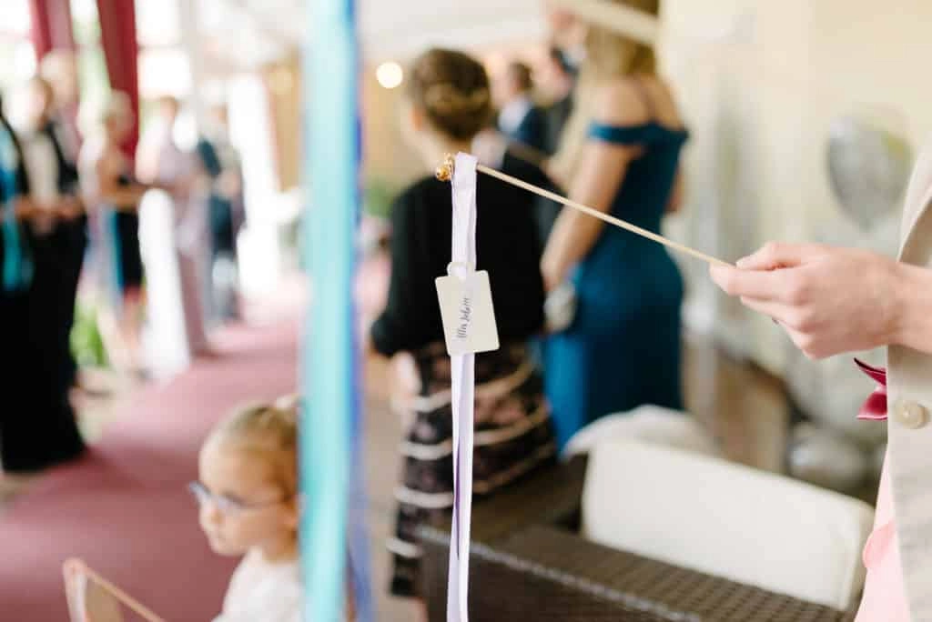 Hochzeitsgäste halten bunte Bänder zur Begrüßung des Brautpaars.