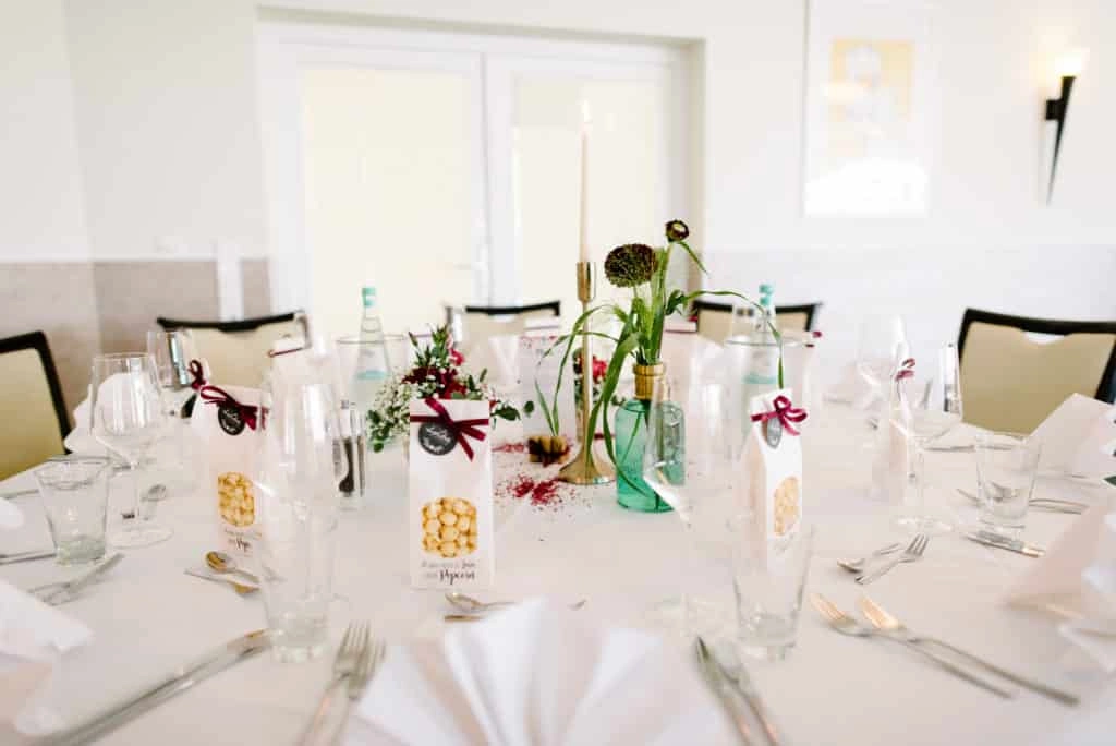 Runder Hochzeitstisch mit Blumen, Kerzen und grünen Vasen.