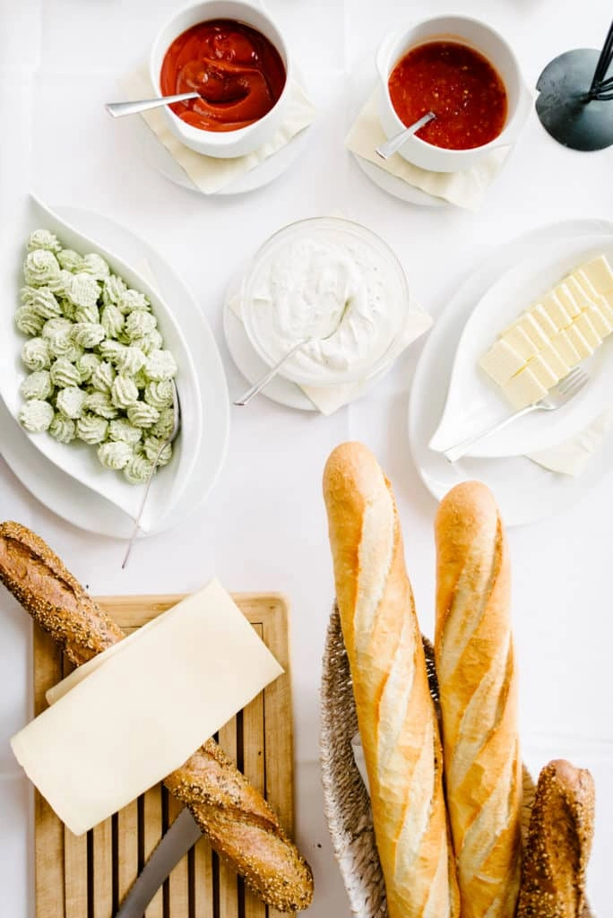 Brot, Käse und kleine Beilagen auf einem gedeckten Tisch.