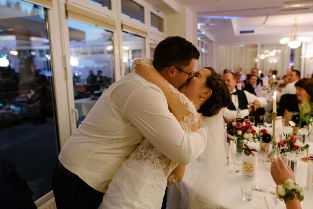 Brautpaar küsst sich neben der Hochzeitstafel.