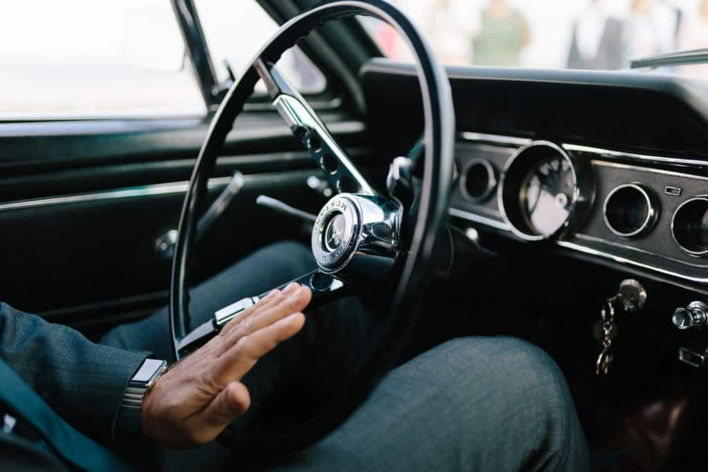 Detail von Lenkrad und Armaturen im Oldtimer mit der Hand des Fahrers.