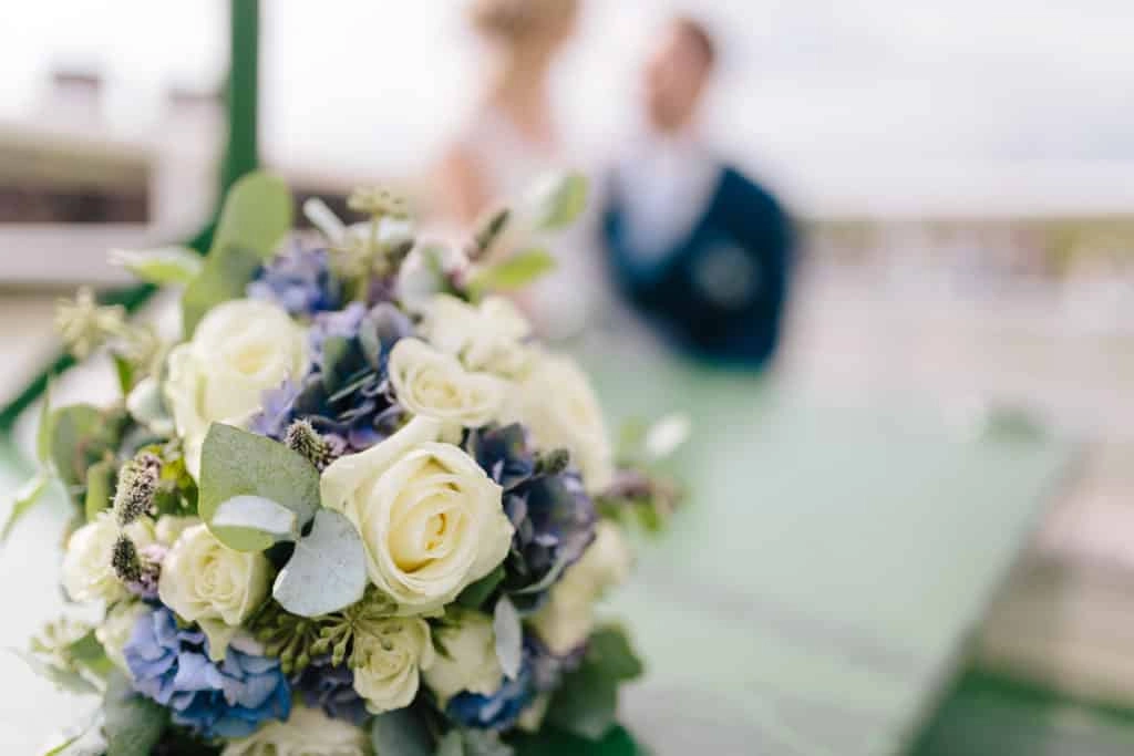 Brautstrauß mit weißen Rosen, blauen Blüten und grünem Blattwerk.