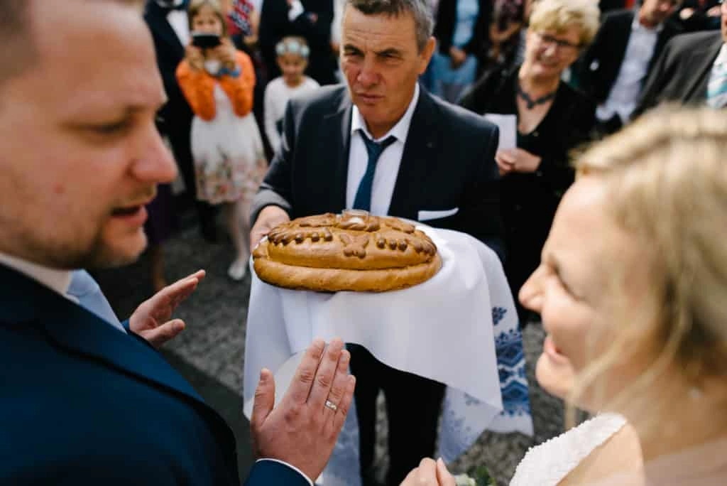 Dem Brautpaar wird draußen ein Kuchen auf einem Tablett gereicht.
