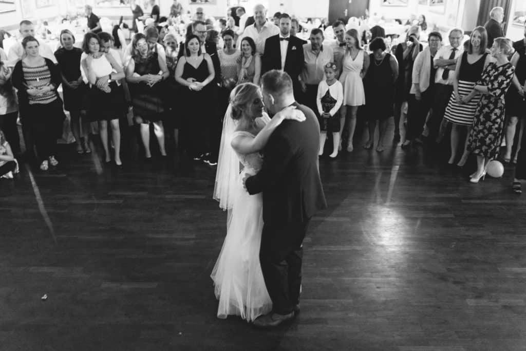 Der Hochzeitstanz vor den Gästen im festlich beleuchteten Saal in Schwarzweiß.