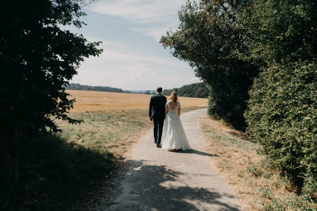 Brautpaar geht Hand in Hand vom Schatten in die offene Landschaft.