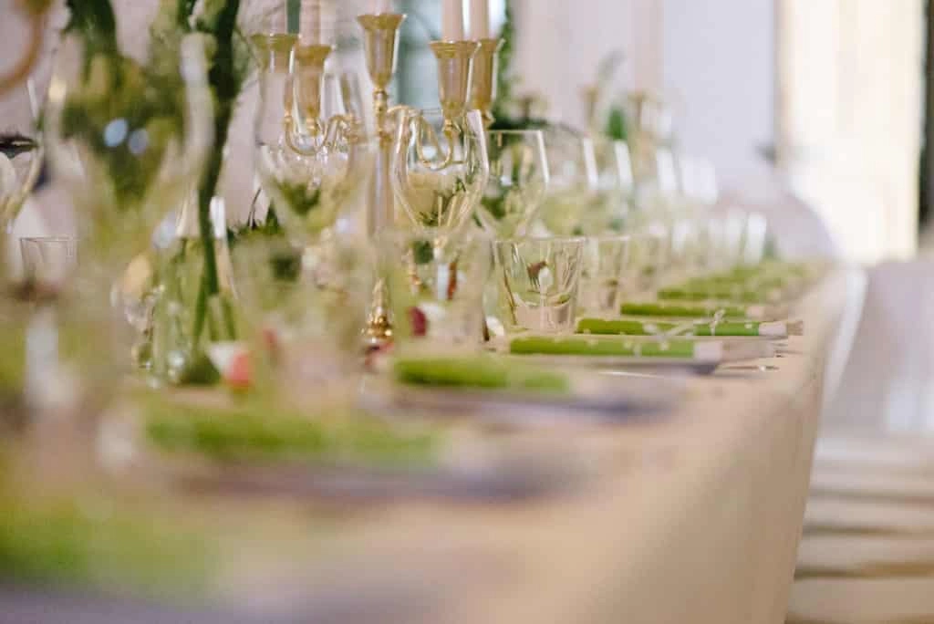 Festlich gedeckte Hochzeitstafel mit schmalen Vasen, Grün und Kerzen.