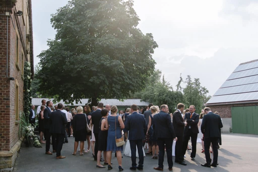 Die Hochzeitsgesellschaft versammelt sich draußen auf dem Hof unter den Bäumen.