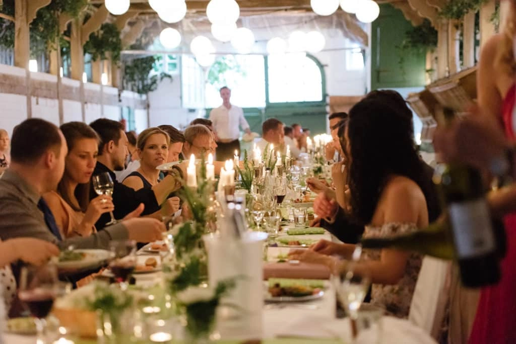 Hochzeitsgäste sitzen an einer langen Tafel mit Kerzen, Blumen und Lichterketten.