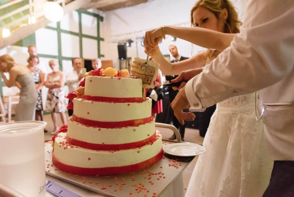 Das Brautpaar schneidet eine mehrstöckige Hochzeitstorte mit roten Fruchtschichten an.