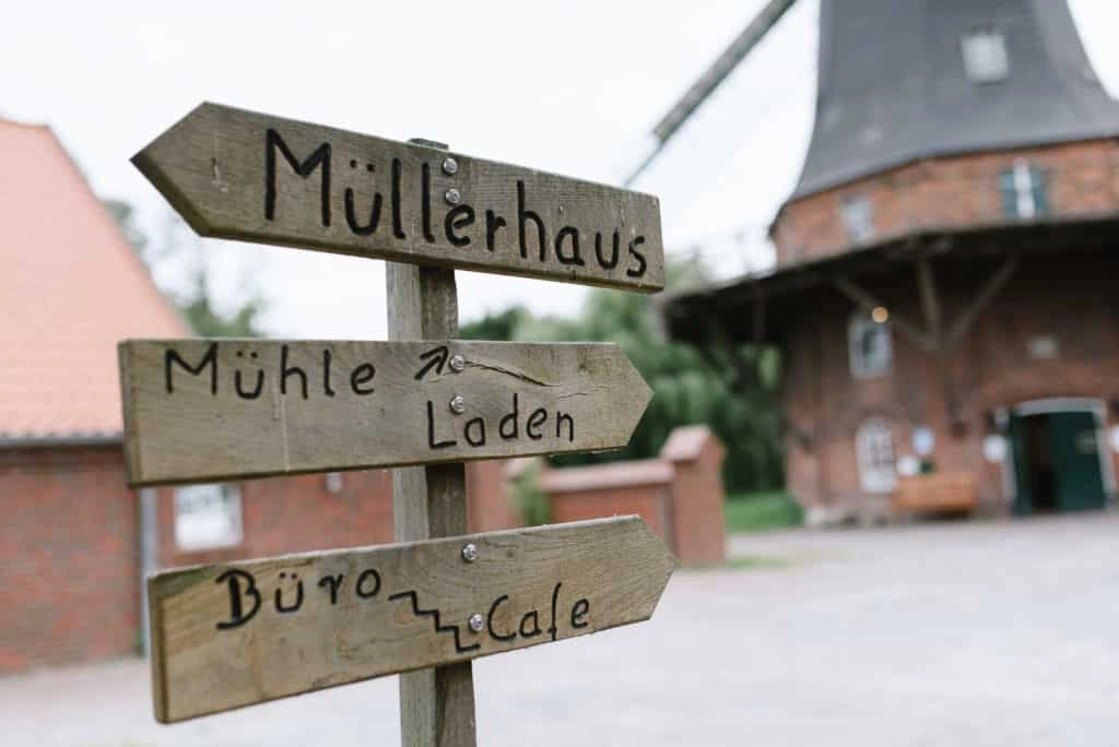Hölzerne Wegweiser vor einer Windmühle.