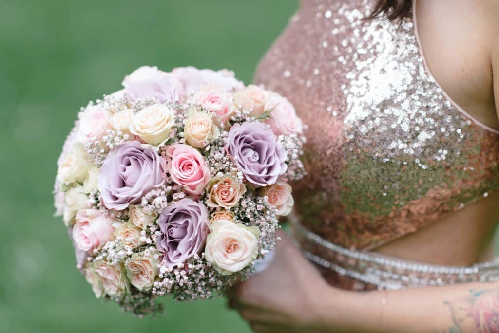 Rosa und violetter Brautstrauß vor dem glitzernden Kleid.