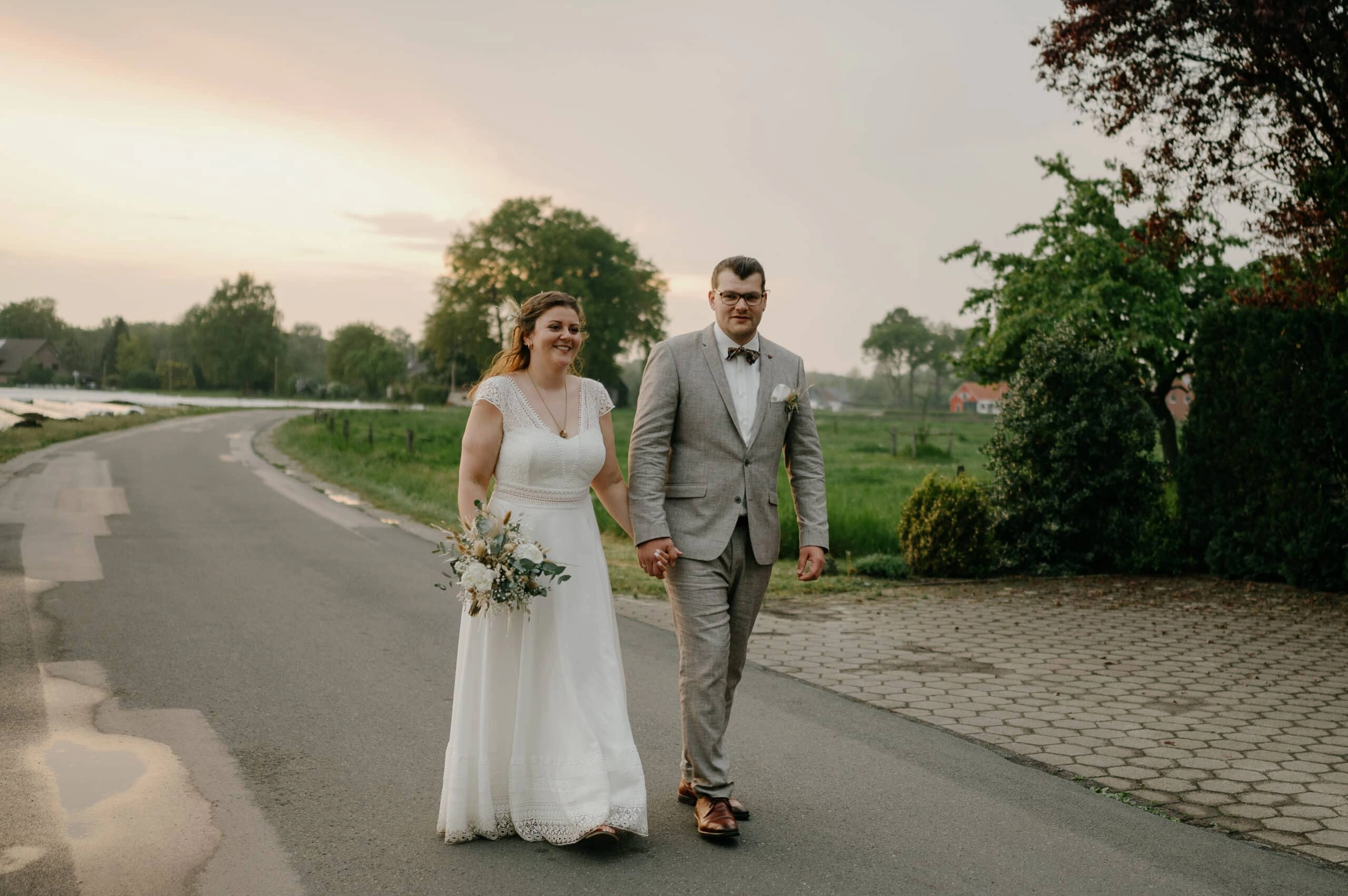 Brautpaar geht Hand in Hand auf einem Landweg.