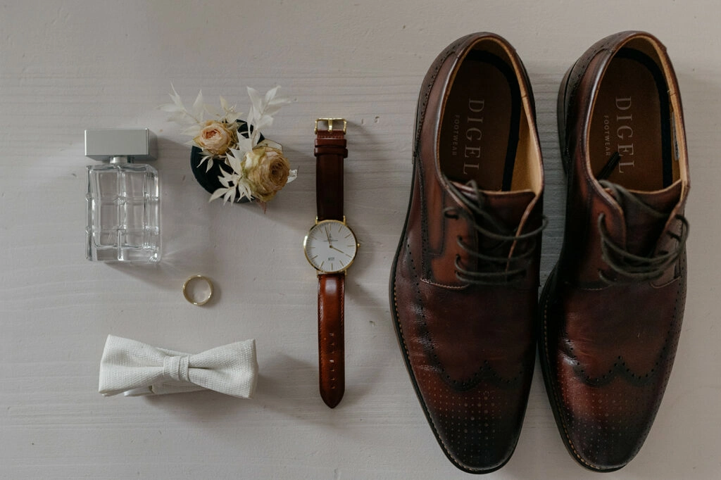 Braune Hochzeitsschuhe mit Fliege, Armbanduhr, Ring und Blumenanstecker.
