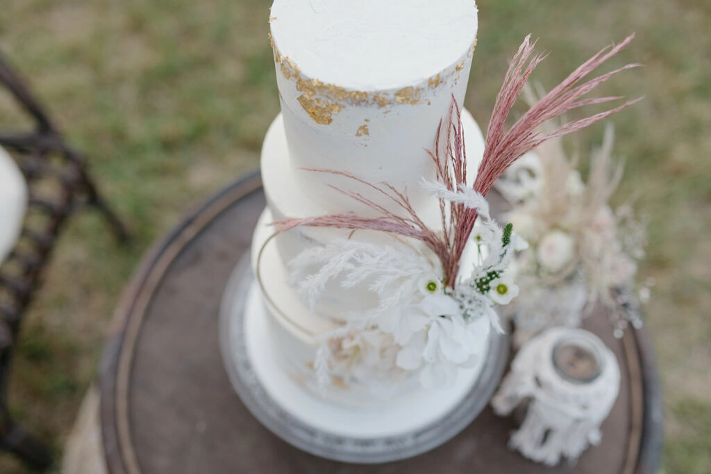 Weiße Hochzeitstorte mit goldenen Akzenten und Trockenblumen, von oben.