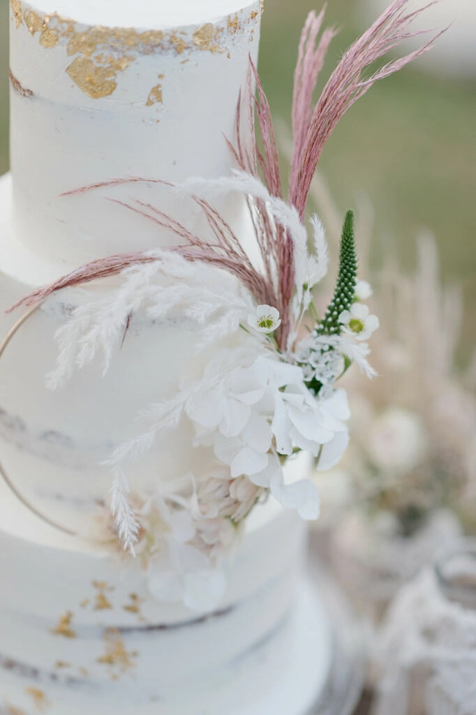 Detail der Hochzeitstorte mit weißen Blüten und rosa Trockenblumen.