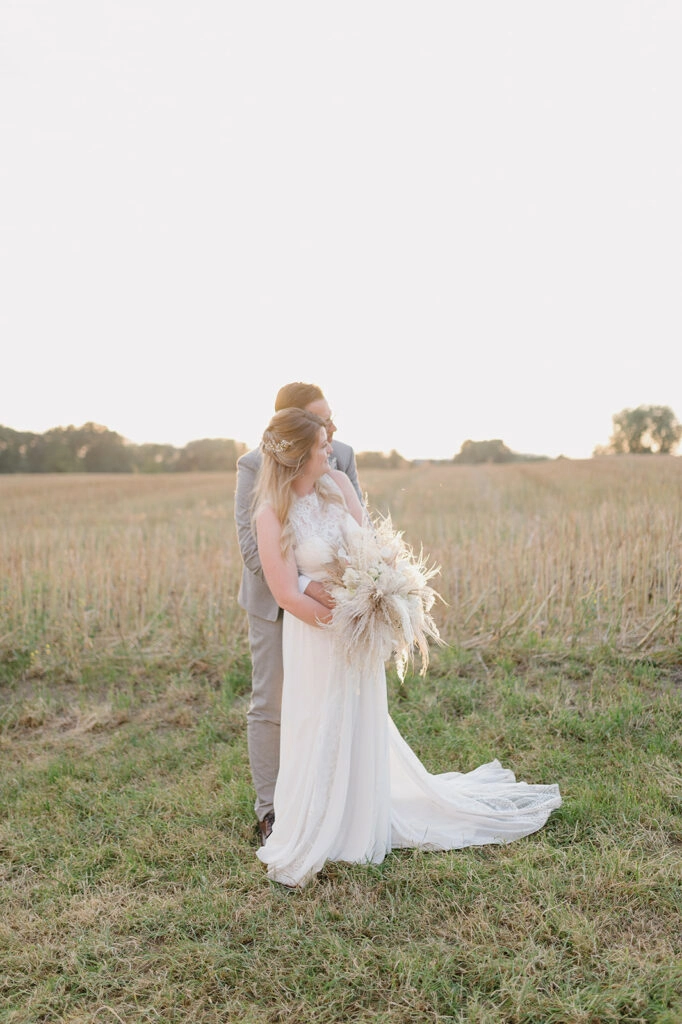 Braut mit weißem Kleid und Trockenblumenstrauß vor einer Wiese.