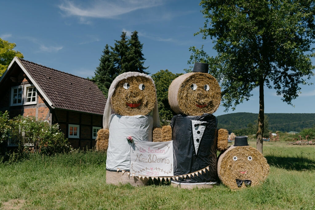 Als Brautpaar und Kind dekorierte Strohballen vor einem Haus.