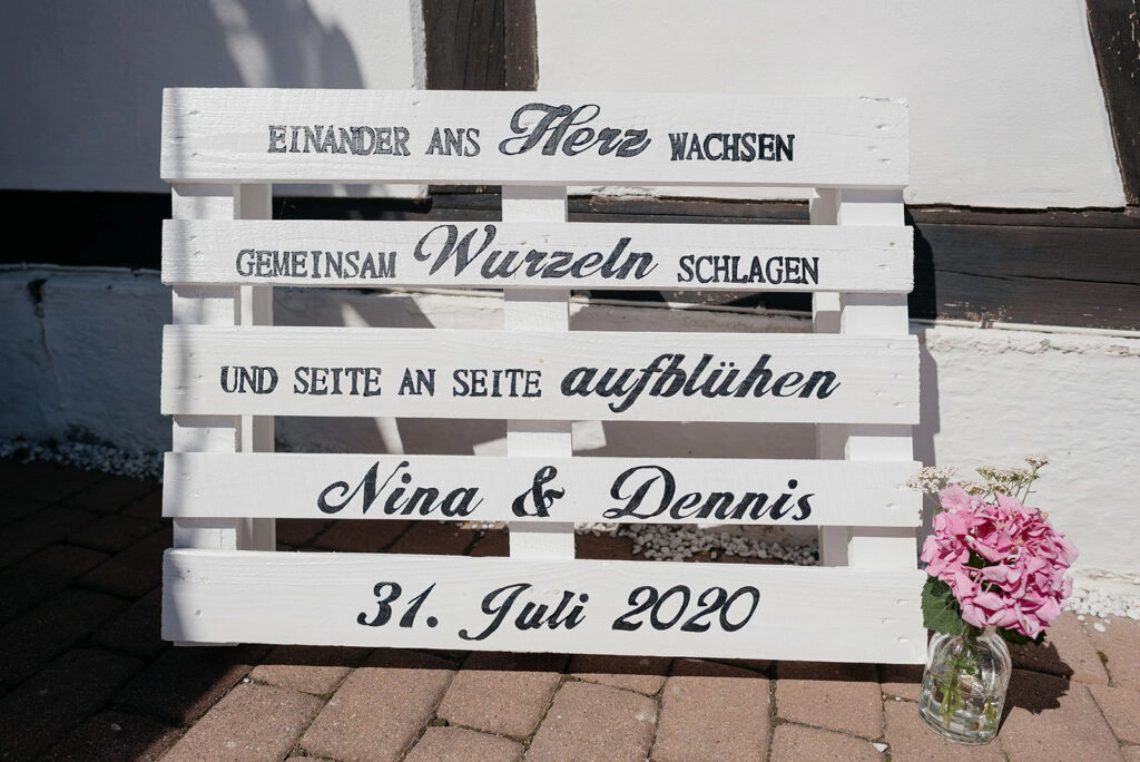 Hölzernes Willkommensschild für die Hochzeit mit rosa Blumen.