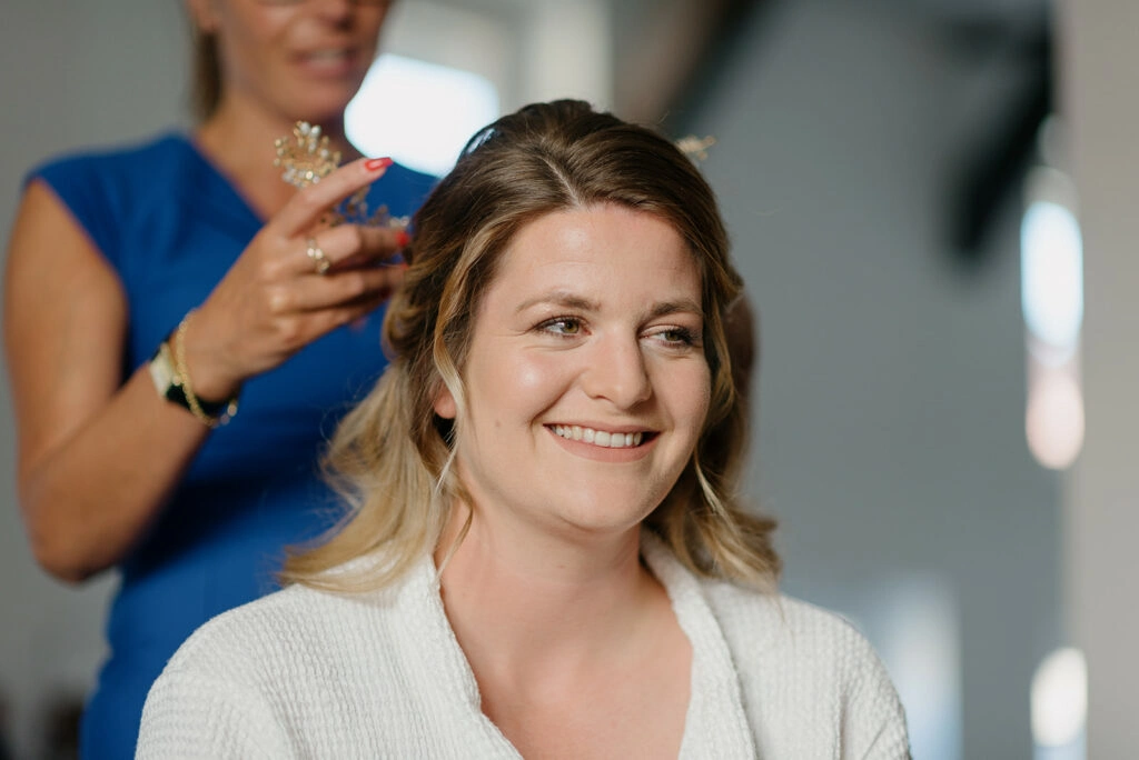 Die Braut lächelt beim Styling ihrer Hochzeitsfrisur.