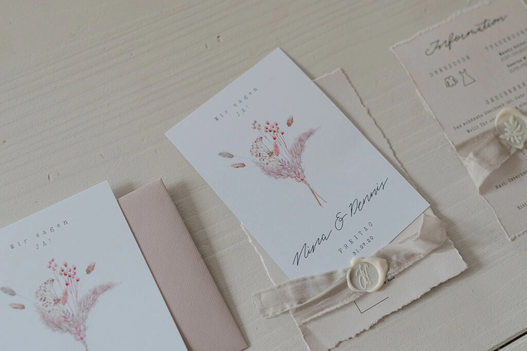 Hochzeitspapeterie mit rosa Blumenmotiven, Bändern und Wachssiegeln.