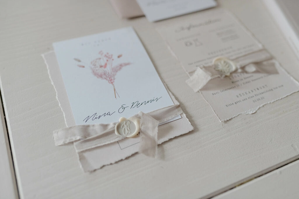 Hochzeitseinladung mit Schleife und Wachssiegel auf einem Tisch.