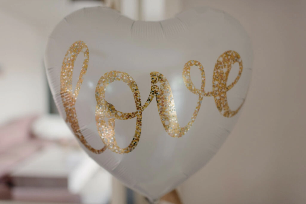 Herzförmiger weißer Ballon mit goldenem Schriftzug „Love“.