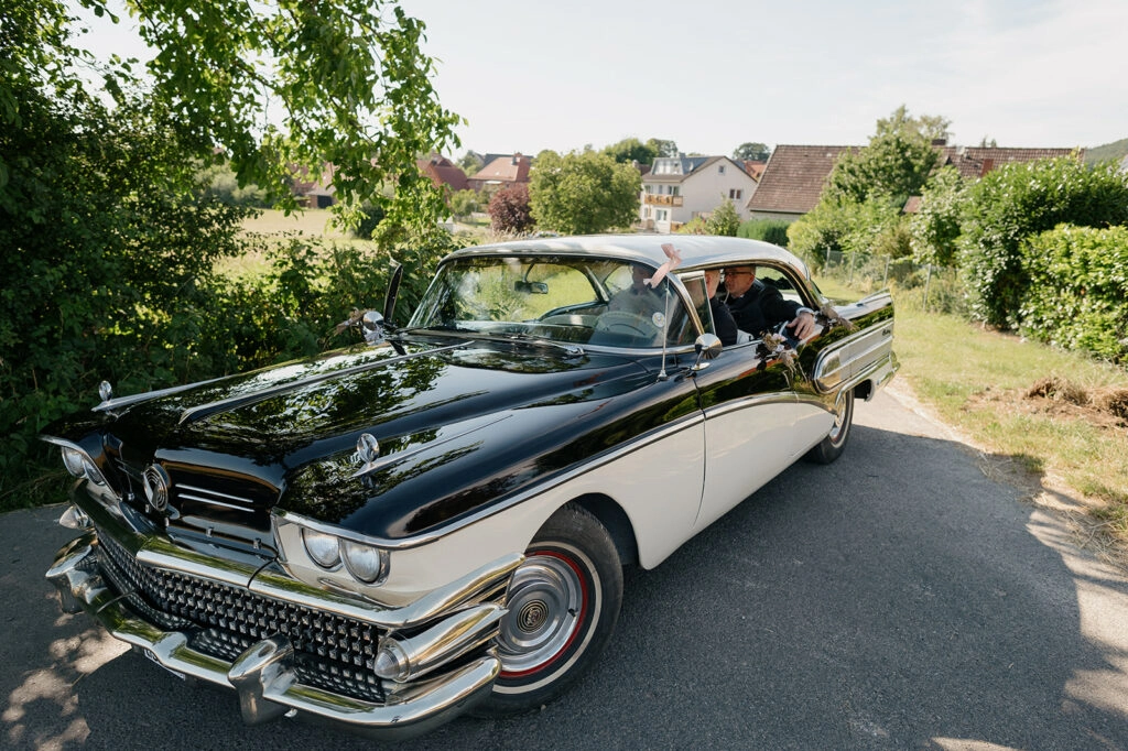 Schwarz-weißer Oldtimer als Hochzeitsauto auf einer Landstraße.