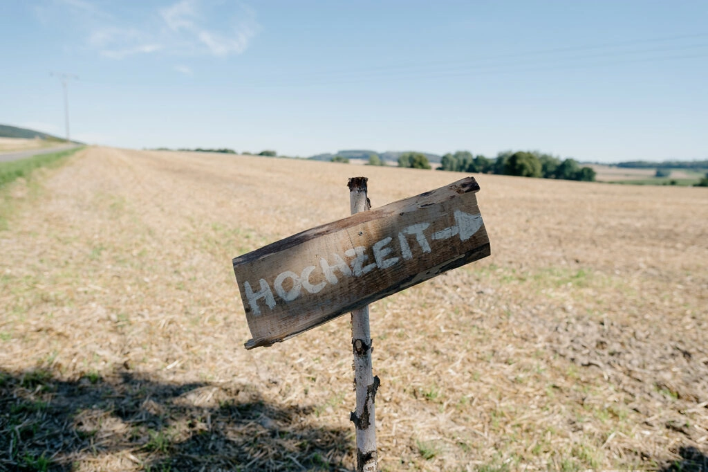 Hölzerner Wegweiser mit der Aufschrift „Hochzeit“ am Feldrand.