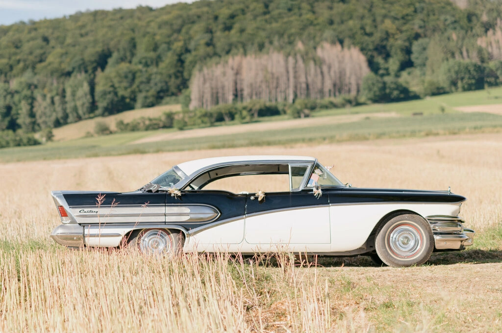 Schwarz-weißer Oldtimer parkt auf einem abgeernteten Feld.
