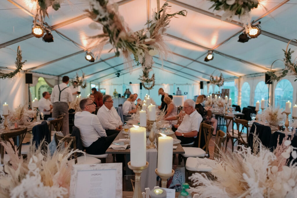 Hochzeitsgäste feiern an langen Tischen im beleuchteten Festzelt.