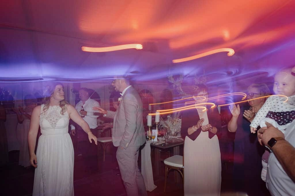 Brautpaar feiert mit seinen Gästen zwischen bunten Lichtspuren.