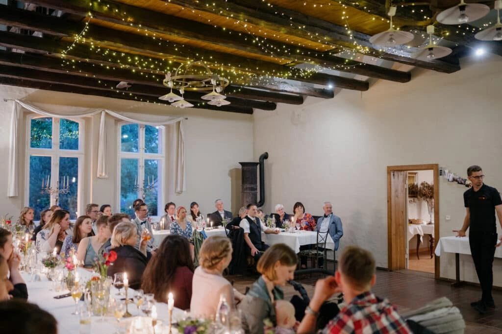 Hochzeitsgesellschaft sitzt an langen Tafeln im Festsaal.