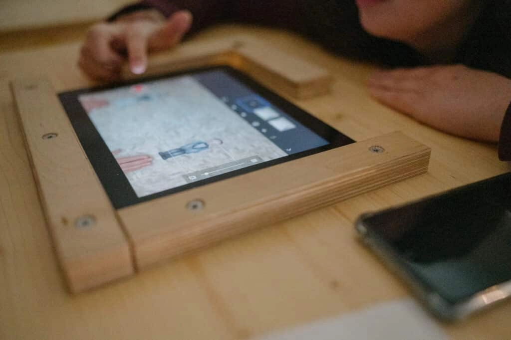 Ein Tablet in einem Holzrahmen liegt auf dem Tisch.