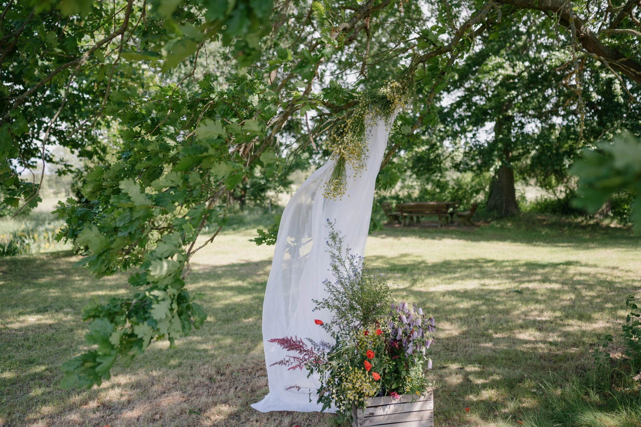 Mit weißem Stoff und Blumen geschmückter Baum für die Trauung.