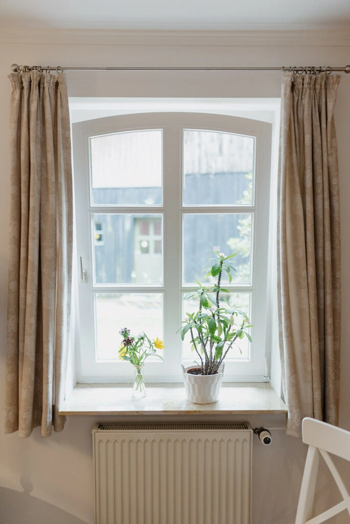 Blumen stehen auf der Fensterbank eines hellen Zimmers.