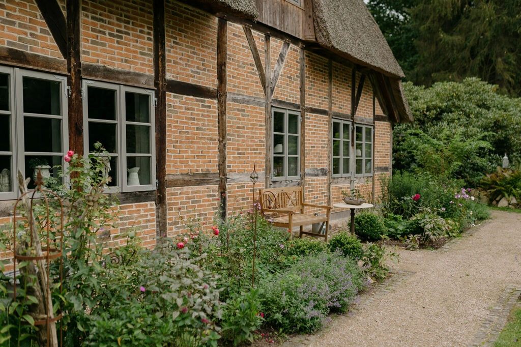 Fachwerkfassade mit Blumen und Sitzplätzen im Garten.